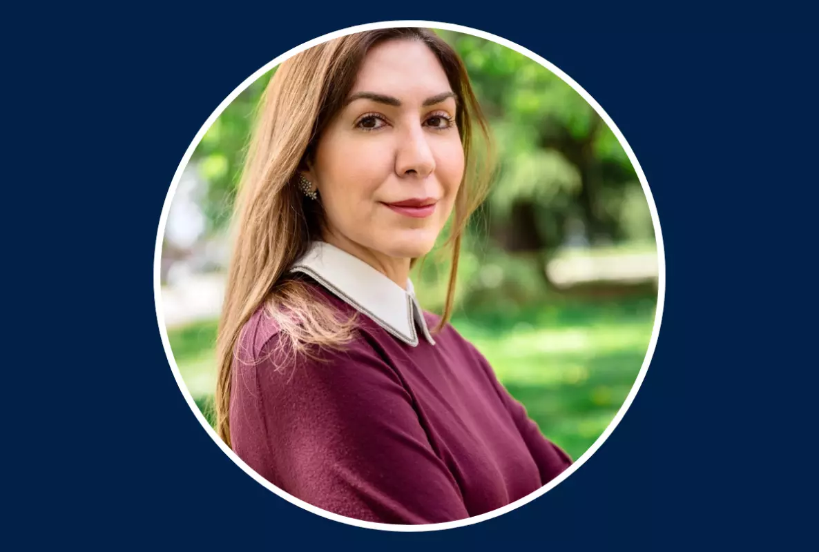 Woman's head and shoulders pictured in a garden and wearing a burgundy sweater